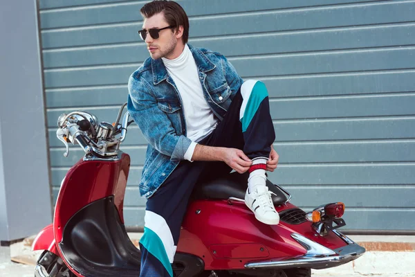 Красивый молодой человек в стильной одежде сидит на винтажном красном скутере — стоковое фото