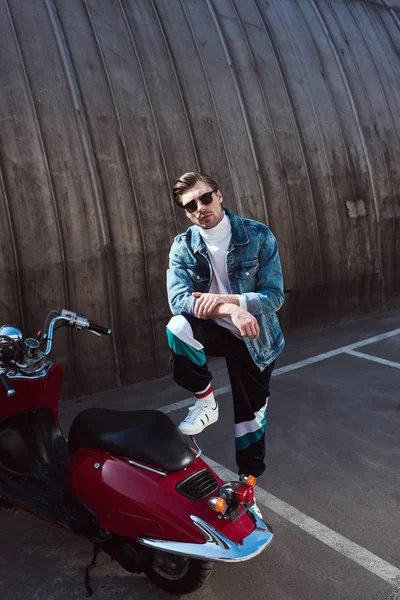 Jeune homme en jean veste élégante avec scooter vintage sur le parking — Photo de stock