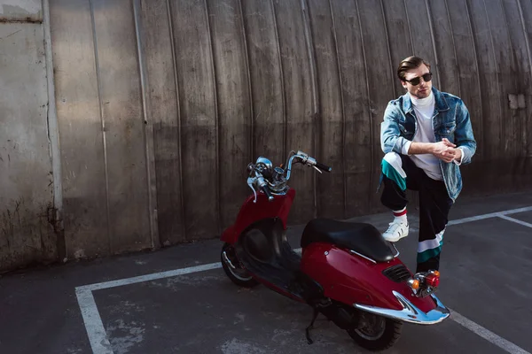 Serious man in stylish denim jacket with vintage scooter on parking — Stock Photo