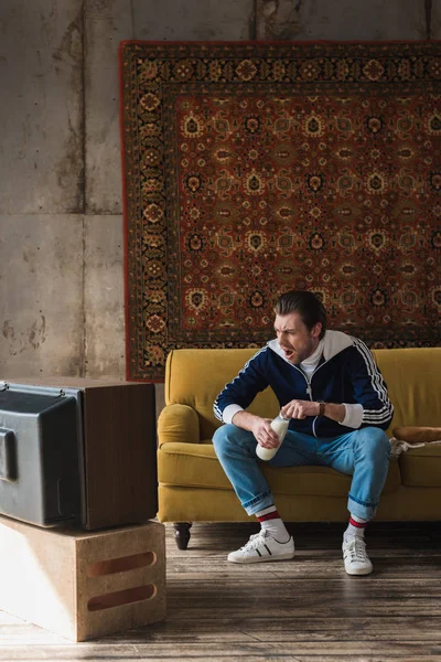 Joven guapo en ropa vintage con botella de leche viendo la televisión - foto de stock