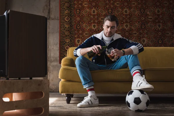 Jovem bonito em roupas vintage com bola de futebol derramando cerveja em caneca — Fotografia de Stock