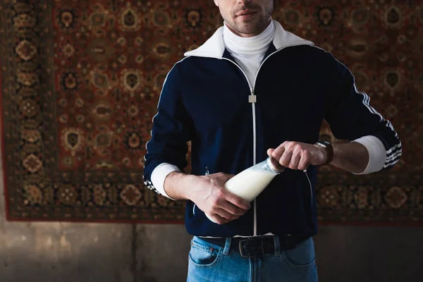 Tiro cortado de jovem em roupas vintage com garrafa de leite na frente do tapete pendurado na parede — Fotografia de Stock