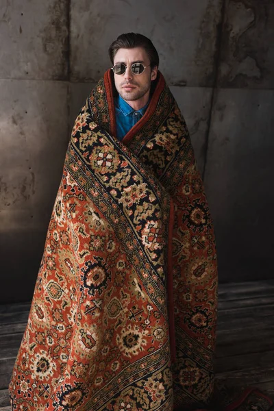 Stylish young man covered in rug in front of concrete wall — Stock Photo