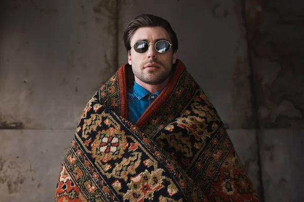 Schöner junger Mann mit Sonnenbrille, mit Teppich bedeckt vor Betonwand — Stockfoto