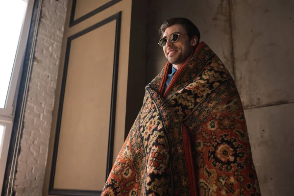 Smiling young man in sunglasses covered in rug — Stock Photo