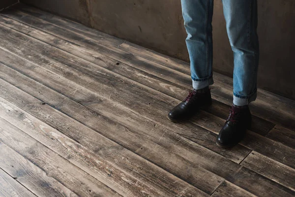 Tiro cortado do homem em jeans elegantes e botas de pé no chão de madeira — Fotografia de Stock