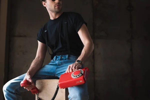 Cropped shot of young man in black t-shirt and suspenders with retro wired red phone — Stock Photo