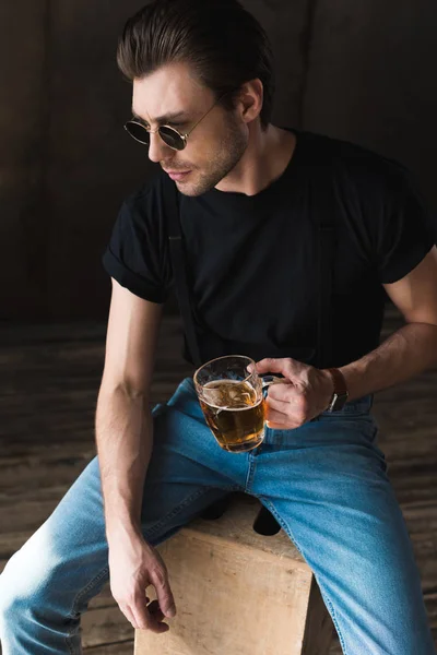 High angle view of handsome young man in black t-shirt and sunglasses holding mug of beer — Stock Photo