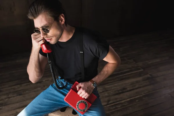 Blick aus der Vogelperspektive auf einen hübschen jungen Mann in schwarzem T-Shirt und Hosenträgern, der mit einem kabelgebundenen Retro-Telefon spricht — Stockfoto