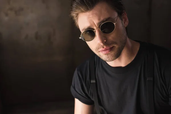 Retrato de cerca del joven guapo en camiseta negra y gafas de sol mirando a la cámara - foto de stock