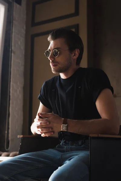 Joven en camiseta negra y gafas de sol sentado en la silla - foto de stock