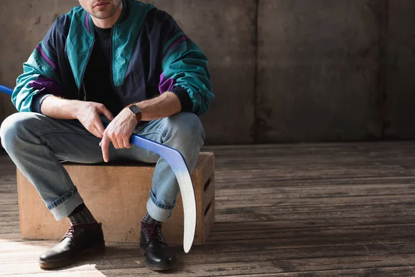 Colpo ritagliato di uomo in giacca a vento vintage con bastone da hockey seduto su scatola di legno — Foto stock