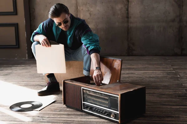 Handsome nostalgic man in vintage windcheater with vinyl record player — Stock Photo