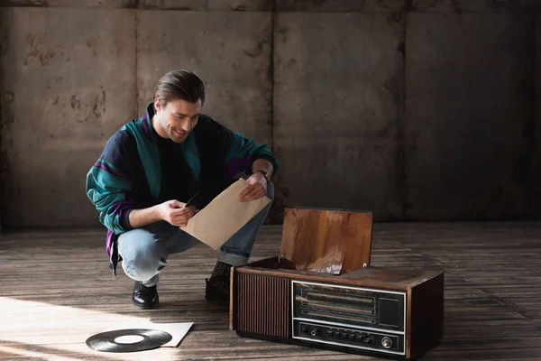 Happy nostalgic young man in vintage windcheater with vinyl record player — Stock Photo