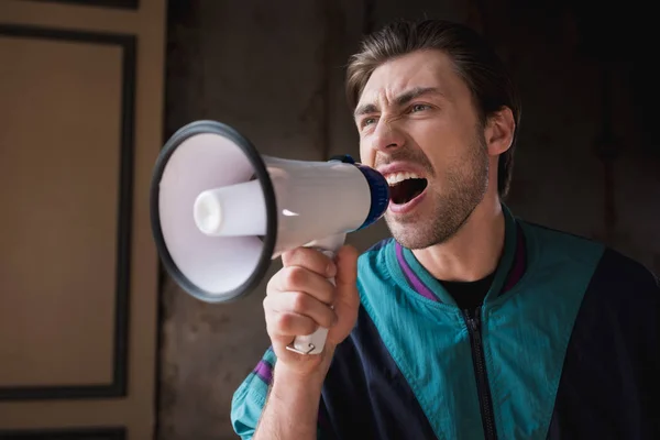Mad young man in vintage windcheater shouting with loudspeaker — Stock Photo