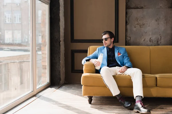 Atractivo joven en traje elegante sentado en el sofá con botella de leche - foto de stock