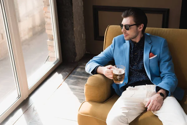 Vista de ángulo alto de joven atractivo en traje elegante sentado en el sofá con taza de cerveza - foto de stock