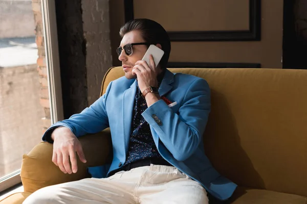 Joven con estilo hablando por teléfono mientras está sentado en el sofá - foto de stock