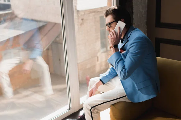 Joven guapo en traje elegante hablando por teléfono mientras está sentado en el sofá — Stock Photo