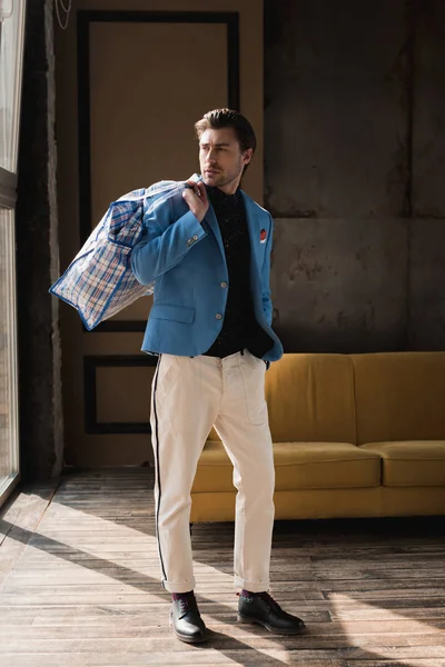 Joven guapo con bolso de lona con cremallera vintage en el hombro en el interior del loft - foto de stock