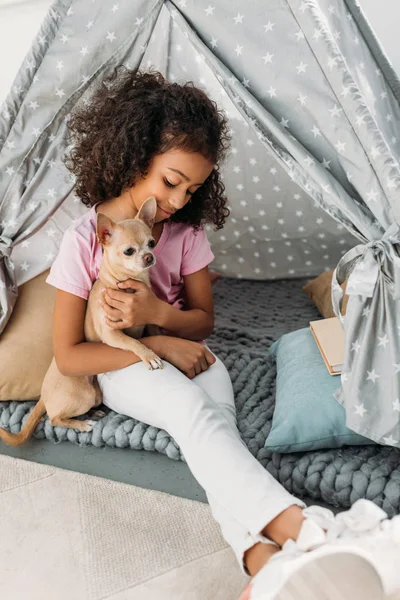 Petit enfant afro-américain mignon avec chihuahua chien en tipi à la maison — Photo de stock