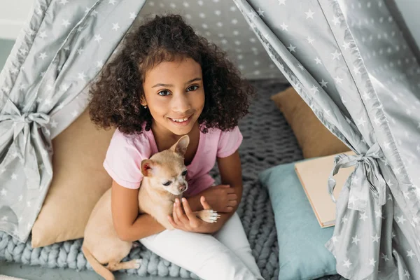 Visão aérea de pouco sorridente criança americana africana com cão chihuahua em teepee em casa — Fotografia de Stock