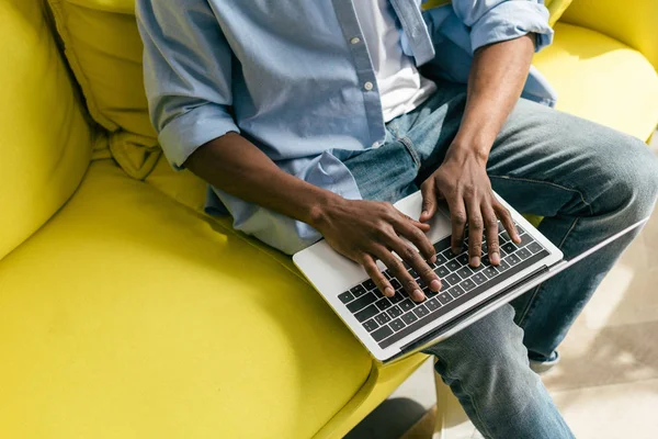 Vue partielle de l'homme afro-américain tapant sur un ordinateur portable sur un canapé à la maison — Photo de stock