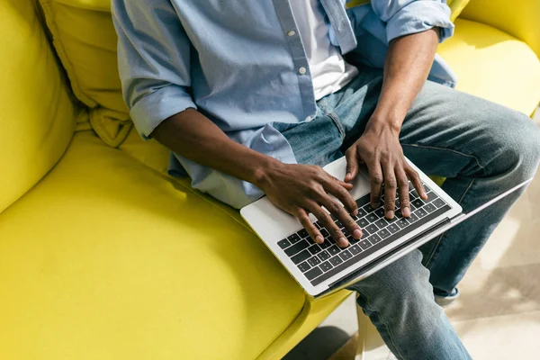 Vista parziale dell'uomo afro-americano che digita sul computer portatile sul divano di casa — Foto stock