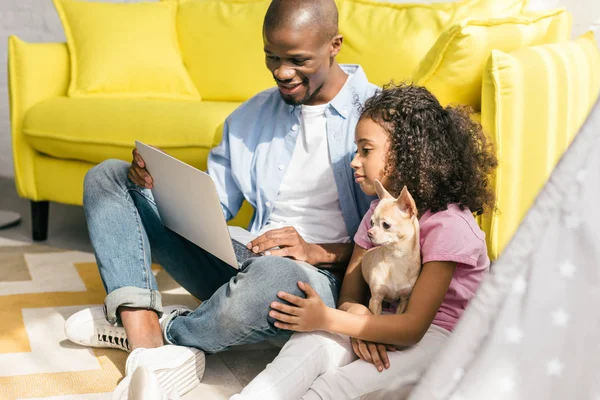 Afro-americano pai e pequena filha com cão usando laptop juntos em casa — Fotografia de Stock