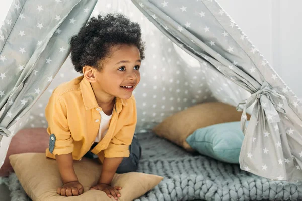 Pequeño niño afroamericano sonriente en tipi en casa - foto de stock