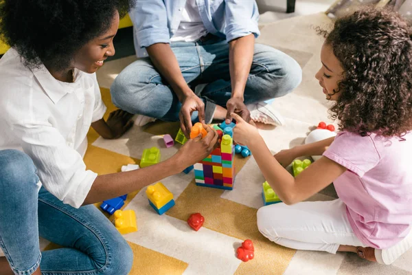 Vue partielle de la famille afro-américaine jouant avec des blocs colorés ensemble sur le sol à la maison — Photo de stock