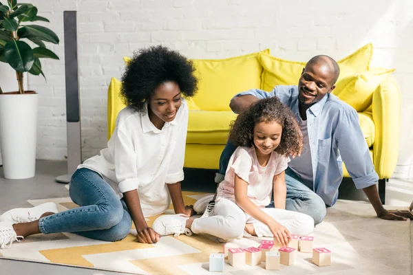 African american parents and daughter playing with wooden blocks together on floor at home — Stock Photo