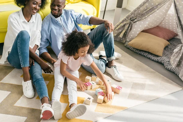 Afroamericanos padres e hija jugando con bloques de madera juntos en el suelo en casa - foto de stock