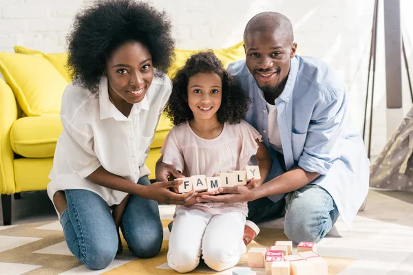 Afrikanisch-amerikanische Eltern und Tochter halten zu Hause Holzklötze mit Familienaufdruck zusammen auf dem Boden — Stockfoto