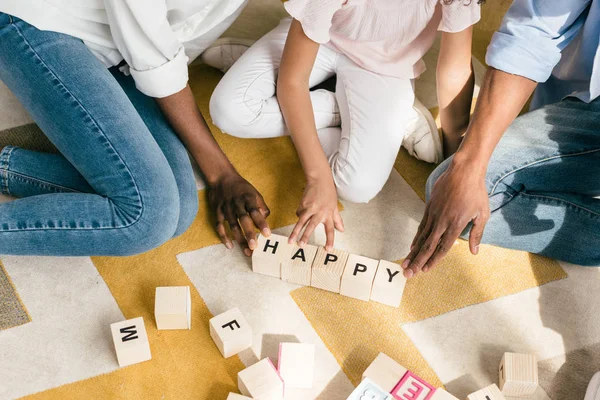 Teilansicht afrikanisch-amerikanischer Eltern und Tochter auf dem Boden sitzend mit fröhlicher Inschrift auf Holzklötzen zu Hause — Stockfoto