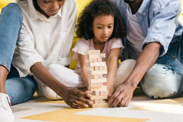 Vista parziale dei genitori afro-americani e la figlia a giocare blocchi torre di gioco insieme a casa — Foto stock