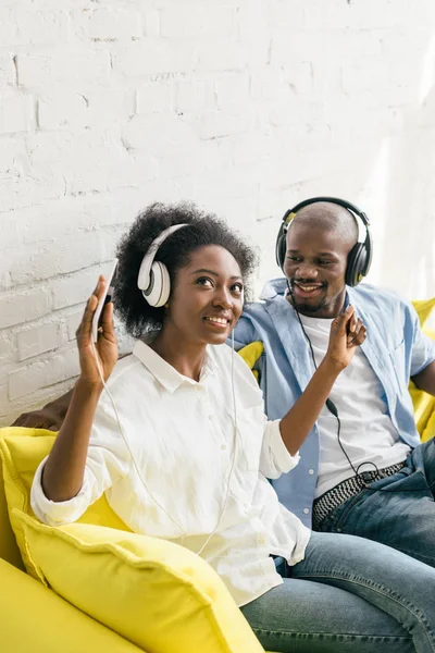 Afro-américaine écouter de la musique dans les écouteurs tout en se reposant sur le canapé à la maison — Photo de stock