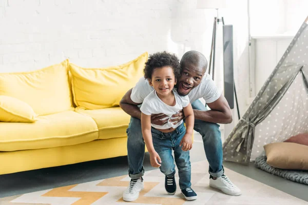 Hombre afroamericano feliz jugando juntos con su pequeño hijo en casa - foto de stock