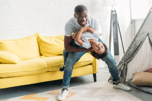 Hombre afroamericano feliz jugando juntos con su pequeño hijo en casa - foto de stock