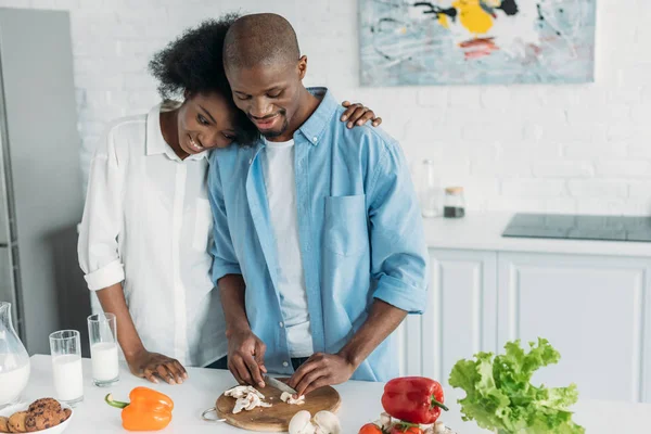 Mujer afroamericana mirando marido cocina desayuno en cocina en casa - foto de stock