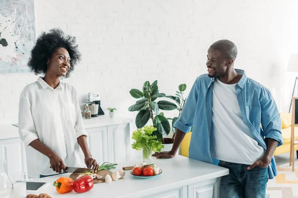 Africano americano hombre mirando esposa cocina desayuno en cocina en casa - foto de stock