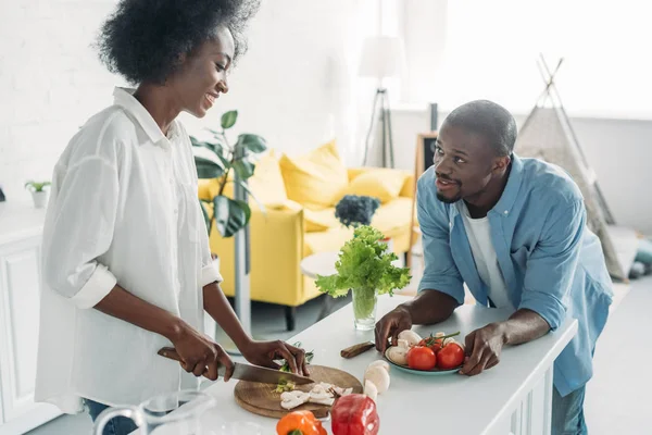 Afro-américain homme regardant femme cuisine petit déjeuner dans la cuisine à la maison — Photo de stock
