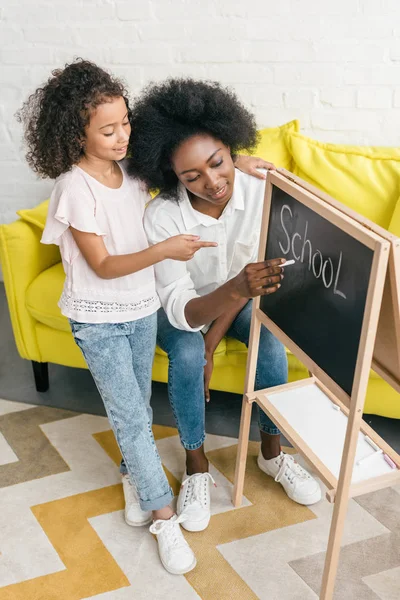 Mujer afroamericana estudiando junto con su hija en casa - foto de stock