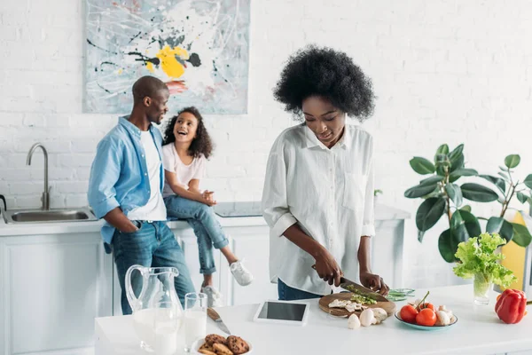 Foco seletivo da mulher africana americana cozinhar café da manhã com a família atrás no balcão na cozinha em casa — Fotografia de Stock