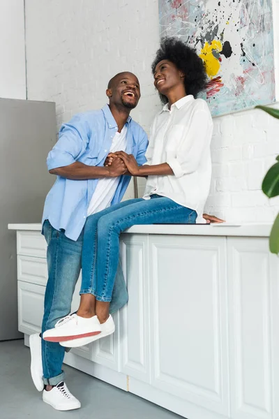 Feliz africano americano pareja cogido de la mano en cocina en casa - foto de stock