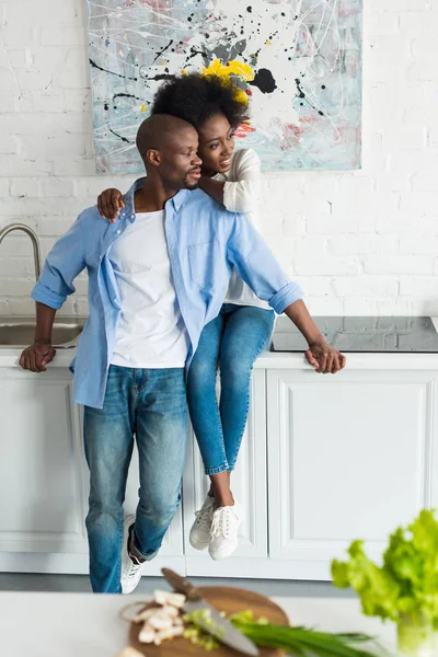 Happy african american woman hugging husband in kitchen at home — Stock Photo