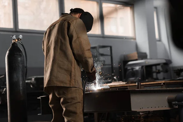 Visão traseira de fabricação de metal de solda trabalhador com faíscas na fábrica — Fotografia de Stock