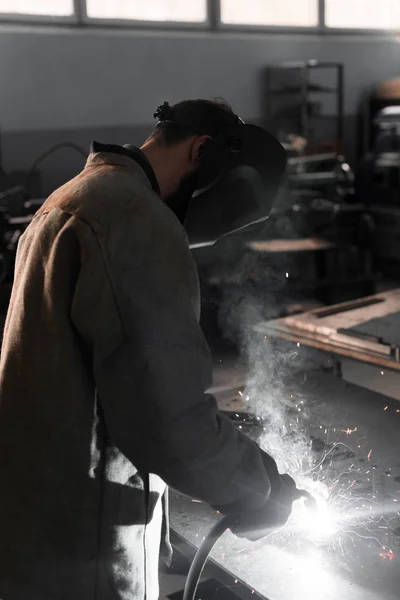 Vista laterale del lavoratore di fabbricazione saldatura del metallo con scintille in fabbrica — Foto stock