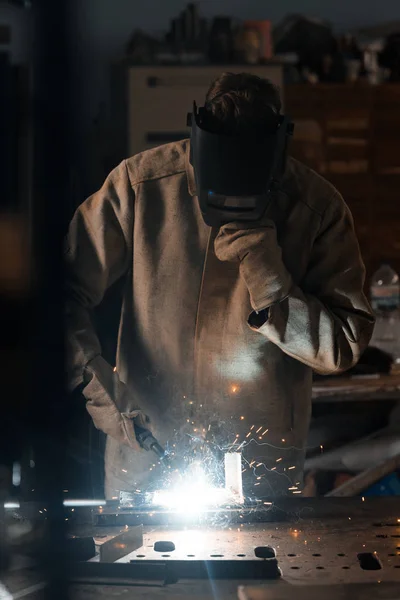 Vista frontal del soldador en máscara de protección que trabaja con metal en fábrica - foto de stock