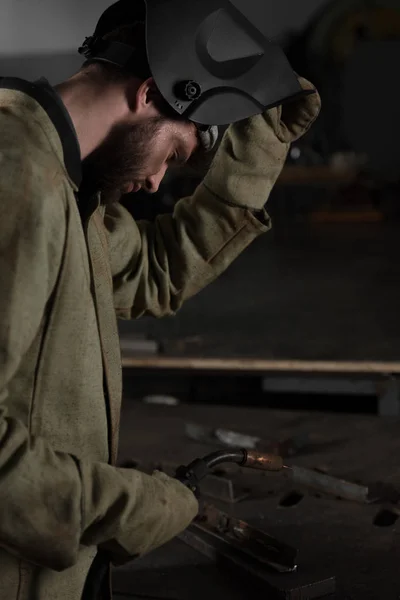 Seitenansicht des Schweißers, der eine Schutzmaske hochzieht, um sich seine Arbeit anzusehen — Stockfoto